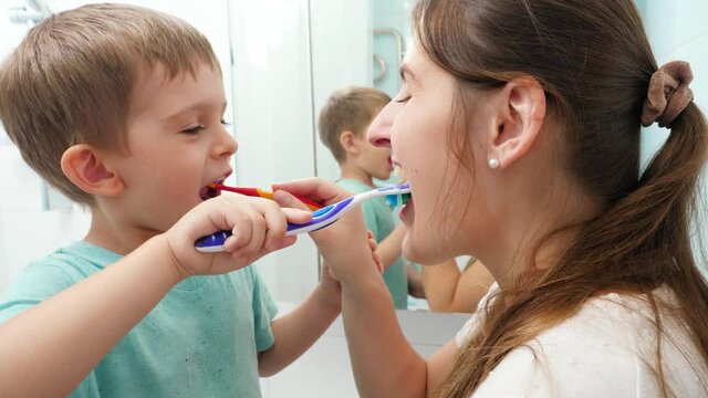 Smiling little boy with young mother brushing teeth and cleaning mouth with toothbrushes to each other. Family having fun while taking care of teeth hygiene and healthcare