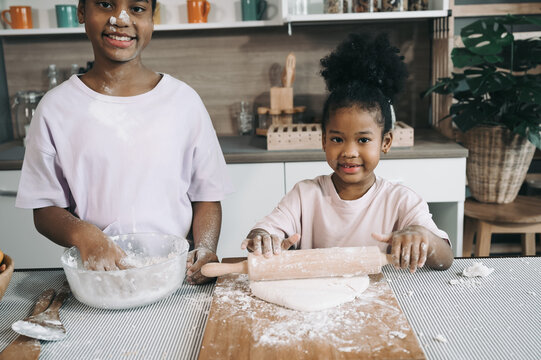 Happy child black skin with sister thresh flour with rolling pin in kitchen