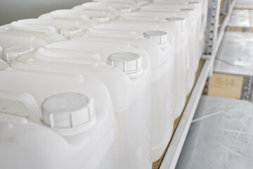 A lot of white plastic cans are lined up on the shelves of the warehouse. Gallons filled with clear liquid