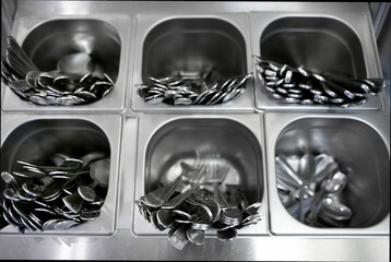 Tray with forks, spoons and knives in the public dining room. Metal cutlery for food. Close-up.