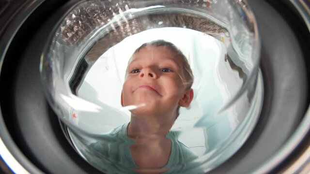 Funny smiling toddler boy looking inside drum of washing machine