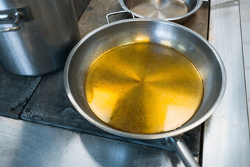 Gray stylish aluminum cookware on the stove in the dining room. A round frying pan is filled with vegetable oil or fat. Cooking.