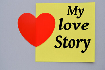 MY STORY LOVE, written on a yellow square paper with a decorative heart, grey background. Happy Valentine's day February