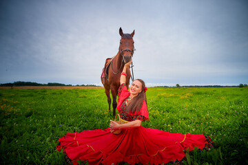 A woman in a bright Gypsy dress and image with a horse in a field with green grass. A model or...