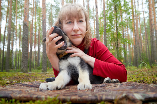 A girl in a red sweater playing with a small German shepherd puppy in the woods