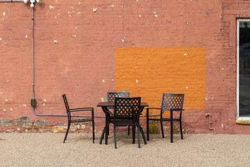 Outdoor dining set in front of a shabby chic old orange and  red color painted brick wall background with an uneven artsy distressed appearance and deterioration