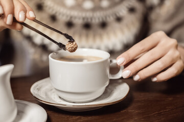 Woman puts a piece of brown cane sugar in a mug of coffee. The concept of healthy eating and excess of glucose and fast carbohydrates