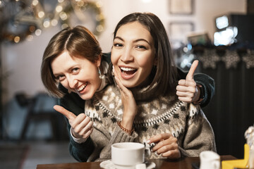 Two female friends hug and have fun sitting in a cafe at the christmas time. Friendship and social distance concept