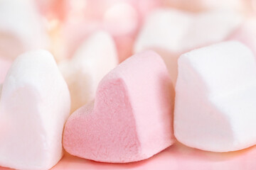 Pink and white marshmallows in the shape of hearts on a pink abstract background with bokeh.