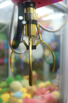 Claw capture device on background of colorful soft toys in Japanese arcade machine games centre.