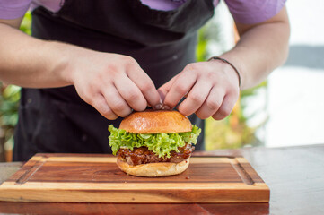 man preparing perfect burger with artisan bread on wooden board with double meat and sauce, fast food