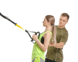 Coach helping young woman to train with TRX straps on white background