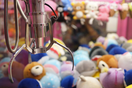 Claw capture device on a background of colorful soft toys in Japanese arcade machine games center.
