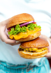 beautiful woman holding delicious burgers with extra cheese in nature, prepared delicious fast food