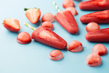 Delicious homemade strawberry popsicles with colorful sticks on blue backgound.