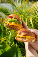 holding delicious burgers with extra cheese in nature, prepared delicious fast food