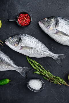 Dorado or seabream fish set with herbs for grill uncooked  on black stone textured table top view.