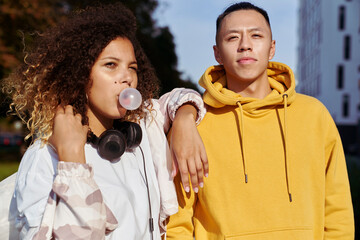 Young couple standing and woman making bubble gum balloon
