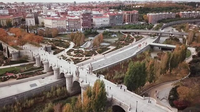 Spain Madrid capital drone shot aerial look view from above city Puente de Toledo Bridge Manzanares river bush art ornaments park sunny day autumn flying down and towards