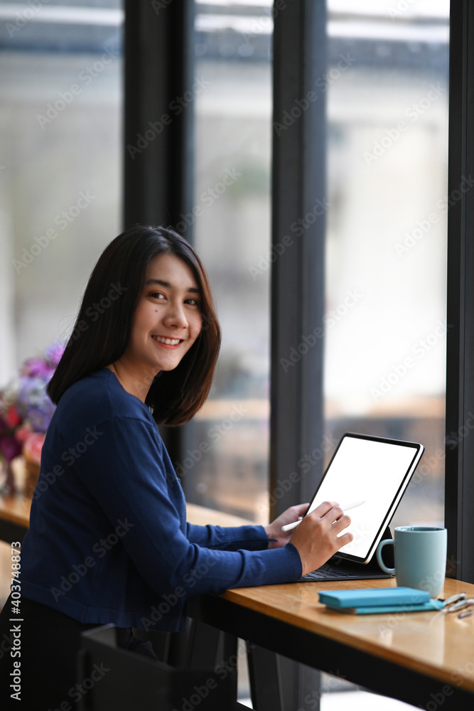 Poster portrait of female college student using tablet computer and smiling at camera while sitting in libr