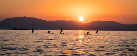 Stand up paddle boarders SUP silhouettes on the water of the sea. Evening, sunset at sea. Active rest on the sea