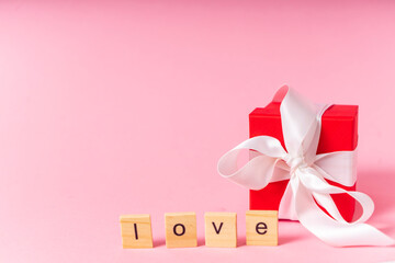 small red gift box with white ribbon and bow on pink background. copyspace. banner. the concept of a gift for the day of all lovers or mother's day