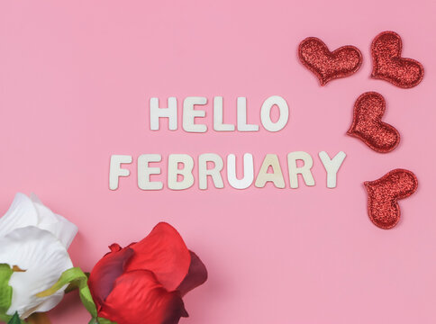flat lay of wooden letters HELLO FEBRUARY  with  red and white roses, red glitter hearts on pink background. Greeting new month and Valentine's day.