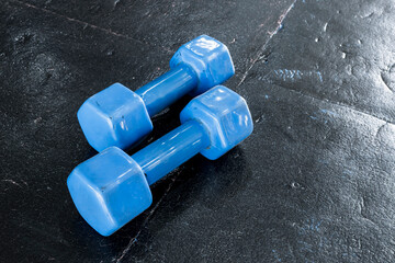 A pair of blue hard plastic hex dumbbells lying on the rubber matted floor of a gym or health club.