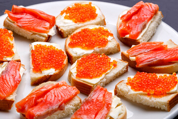 Bruschettes with butter and red caviar and salmon on a white plate.