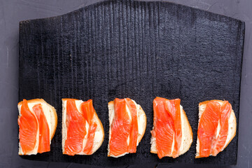 Bruschettes with butter and salmon on a black board on a gray concrete background Copy space.
