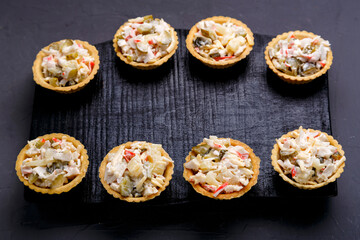 Salad tartlets with pineapple and shrimps on a black wooden board on a gray concrete background.