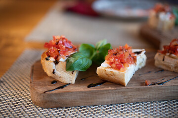 Italian bruschetta with fried tomatoes, mozzarella and basil on a cutting board.