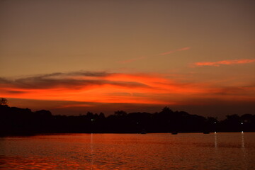 Naklejka premium Picture of a sun setting behind a dense forest area followed by mountains.