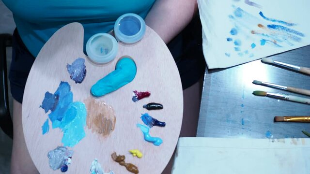 a talented artist takes oil paints with a brush from a wooden palette for drawing. draws on canvas. the view from the top.