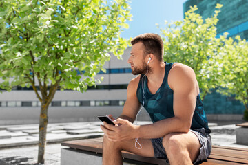fitness, sport and technology concept - young athlete man with earphones and smartphone listening to music outdoors
