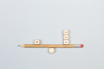 Cubos de madera con el signo positivo y negativo colocados en forma de balanza sobre ubn fondo gris aislado. Vista superior. Copy space. Concepto: Equilibrio entre los pro y los contra