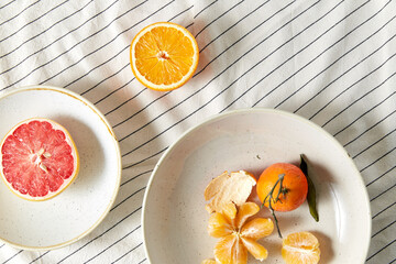 food, healthy eating and fruits concept - close up of mandarin, grapefruit and orange on plates over drapery