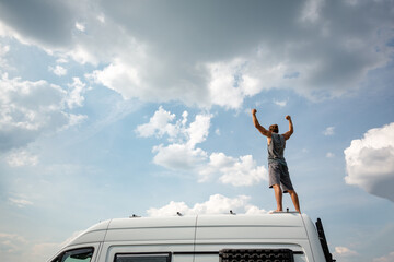 Man with raised arms standing on top of his camper van