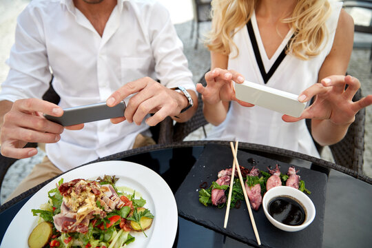 technology and people and concept - close up of couple with smatphones taking picture of food at restaurant terrace