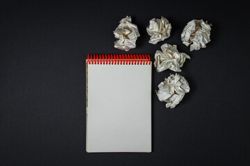 A blank sheet of notebook with crumpled paper around. Crumpled paper on a black background. Creative crisis. Lack of ideas. Background for lettering or logo