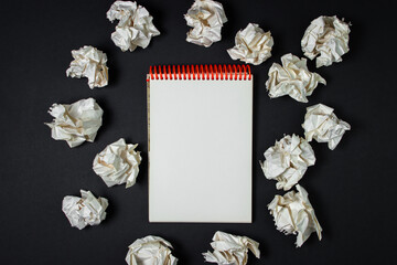 A blank sheet of notebook with crumpled paper around. Crumpled paper on a black background. Creative crisis. Lack of ideas. Background for lettering or logo