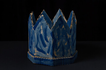 Cardboard crown on a black background. Paper product. Fake crown. A sloppy blue crown. Lie power