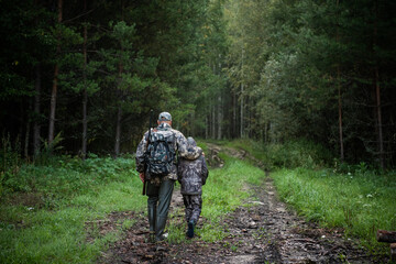 Hunters with hunting equipment going away through rural forest at sunrise during hunting season in countryside. - 403763654
