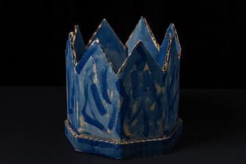 Cardboard crown on a black background. Paper product. Fake crown. A sloppy blue crown. Lie power
