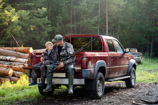 Father and son sitting together in truck outdoors with shotgun hunting gear.