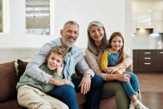 Portrait of happy family spending time at home, grandparents and grandchildren relaxing on sofa in the living room, smiling at camera