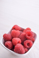 Bowl of fresh raspberries with green leaves on wooden background. Top view