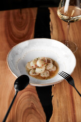 The vertical frame. Restaurant serving delicious scallop crudo and a glass of white wine on a wooden table