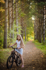 Children girl riding bicycle outdoor in forest smiling.