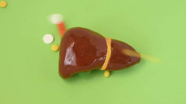 Liver and pills, drugs, medications. Treating of liver diseases concept. Pharmaceutical pills and capsules falling from above on anatomical shape of liver, symbolizing impact of drugs on function